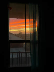 A sunrise from a second floor bedroom window in Arizona, the sky is striated gray-blue and neon orange and yellow